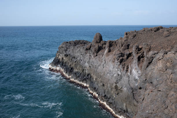 A striking volcanic pebble beach in Lanzarote, Canary Islands, where dark, smooth stones contrast with the deep blue Atlantic Ocean. The rugged coastline, shaped by volcanic activity, meets powerful waves crashing against jagged rocks. A dramatic and untamed seascape, showcasing the raw beauty of nature.