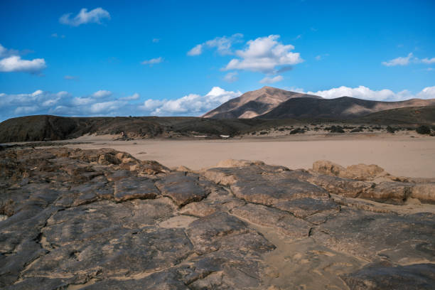 A stunning volcanic landscape in Lanzarote, Canary Islands, featuring black lava rocks and reddish mountains. The arid and wild scenery resembles a lunar environment, a testament to the eruptions that shaped the island. A unique place where nature tells its story through geological formations and earth tones