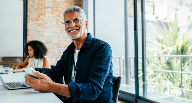 istock Grey-haired businessman using technology in a contemporary office setting, smiling confidently while using modern technology 2198315748