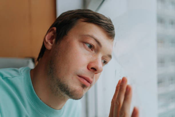 istock Young man suffering from depression looking out the window 2198318729