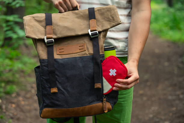 istock Hiker holding a backpack and a red first aid kit, walking on a forest trail, prepared for outdoor adventure. 2198320634