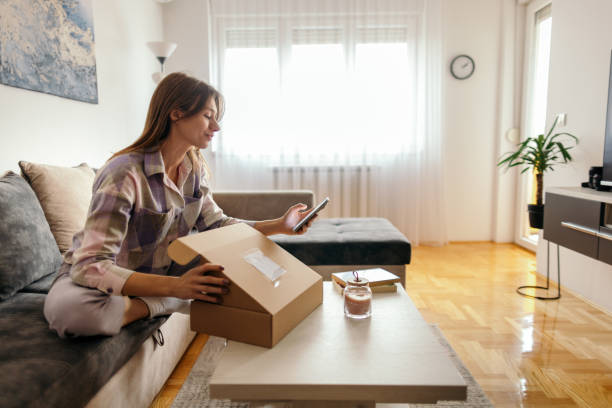 istock Woman using mobile phone and checking and opening  just received package boxes 2198324550