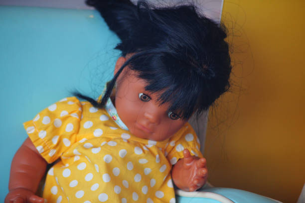 A medium dark skinned doll with black hair and a yellow dress with white dots on it