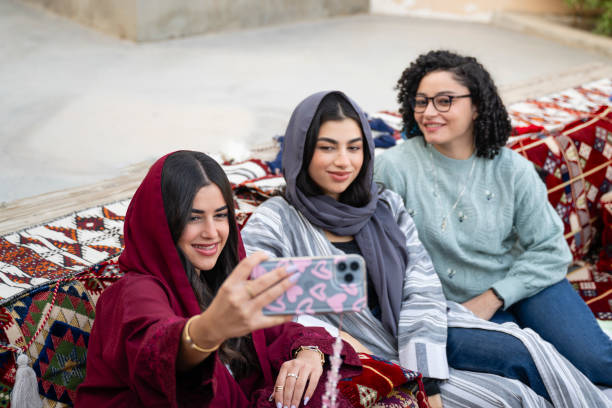 istock Three young women taking selfie on smartphone, sitting on traditional patterned seating in majlis, a traditional Arabic meting space 2198333419