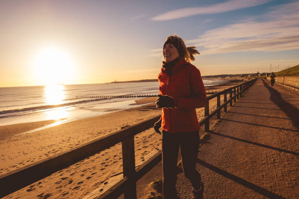 Senior woman running on the pedestrian walkway below the Esplanade just north of Aberdeen, Scotland, as dawn breaks.
