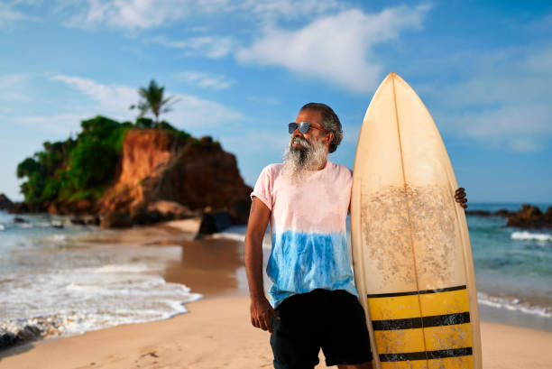 istock Senior ethnically diverse man stands holding surfboard on sunny beach. Active retiree enjoys ocean. Lifestyle of adventurous elder, carefree days, retirement fun. 2198338462