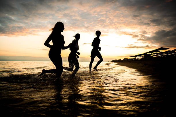 Silhouettes of friends running on the beach during sunset