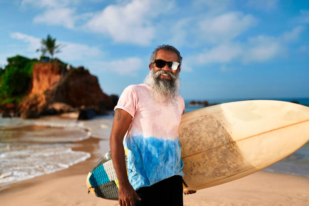 istock Senior ethnic man with surfboard on sandy beach. Mature surfer enjoys active lifestyle, relaxing after work. Retirement, leisure, sport, freedom, ocean view. Healthy aging, golden years, coastal life. 2198340670