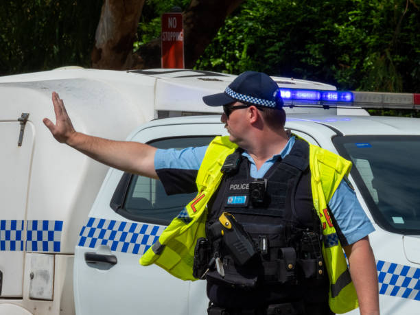 A constable of the New South Wales Police Force on traffic duty directing motor vehicles around two vehicles which had collided at the corner of Carrington Road and Pine Street, Randwick. In the background is the police paddy wagon and No Stopping sign. This image was taken on a hot and sunny morning on 8 February 2025.