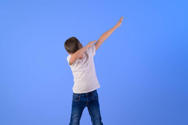 istock Portrait of elementary boy with arms raised dabbing while dancing against isolated blue background 2198342099