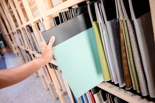 istock Stylist hand choosing turquoise fabric piece from fabric swatch material. Upholstery sample collection hanging on showcase rack. Textile industry for home interior design and furniture finishing decor 2198342321