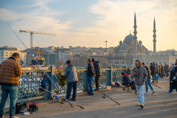 Istanbul, Turkey - 31 January, 2025: Fishermen on the Galata Bridge in Istanbul against the Yeni Mosque backdrop at sunset