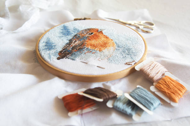 istock cross stitch process in the hoop multicolored bird, white canvas, floss threads on bobbins, needle, needlework and cross stitch concept 2198352147