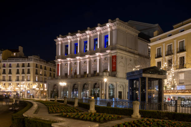 Madrid, Spain - July 12, 2015: Deep blue dusk skies over the warm lamplight of the Plaza de Oriente with locals and tourists enjoying the warm summer evening below the iconic facade of the Teatro Real in the heart of Madrid, Spain's vibrant capital city. Composite panoramic image created from seven contemporaneous sequential photographs.