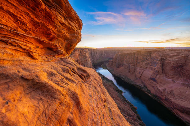 Sunset over the Grand Canyon and Colorado River in Arizona, where dramatic canyon walls glow in golden light. This stunning landscape captures the beauty of the Southwest’s rugged terrain, deep gorges, and winding river, creating a mesmerizing natural wonder.