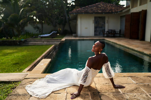 istock Ambiguous gender fluid black bride in white dress sits by villa pool. Sunlight, elegance, diversity. Perfect for pride themes, inclusive weddings, lifestyle blogs. Modern love, identity, celebration. 2198363092