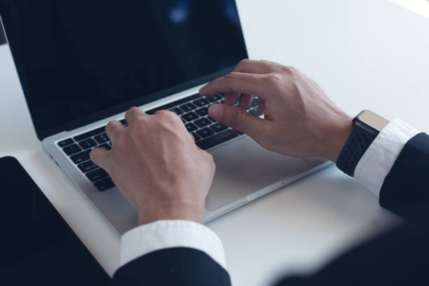 istock Young businessman working on laptop computer on white table at office. Business man hands typing on laptop, online working, surfing the internet, close up 2198368640
