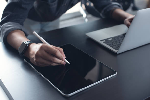istock Business man, graphic designer using stylus pen on digital tablet screen while working on laptop computer on office table. Man in casual ware online working, surfing the internet on tablet pc 2198368641