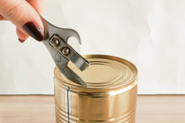 istock A woman's hand opens a tin can with a can opener. Tin cans. Meat, vegetable, fish preserves. 2198373075