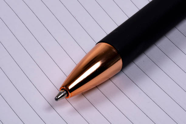 A stylish black and gold pen lies on a sheet of lined paper, showcasing its shiny metallic tip against a backdrop of simple, structured lines.