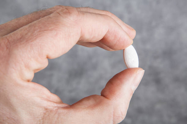istock Man's hand holding white pill on grey background. Focus on pill 2198381710