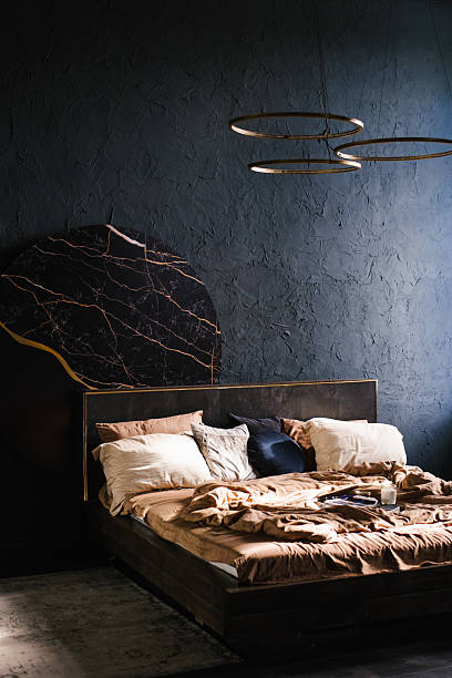 istock Large bed with a black headboard, surrounded by pillows. Bedroom is dark and modern 2198384663