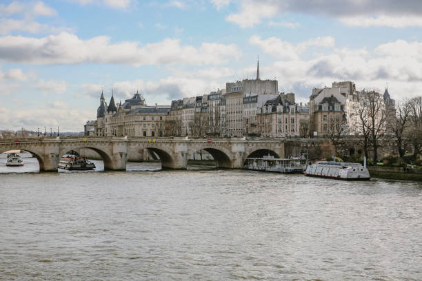 A bridge spans a river Cena in Paris with boats on it. The bridge is over a city with buildings and a church