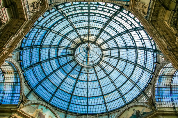 A large dome with a blue sky above it in Milano Italy. The dome is made of glass. There are several people in the background