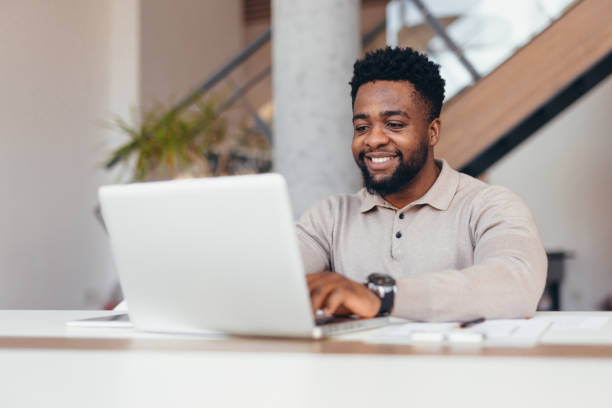 istock Smiling young businessman working on laptop in modern office 2198392848