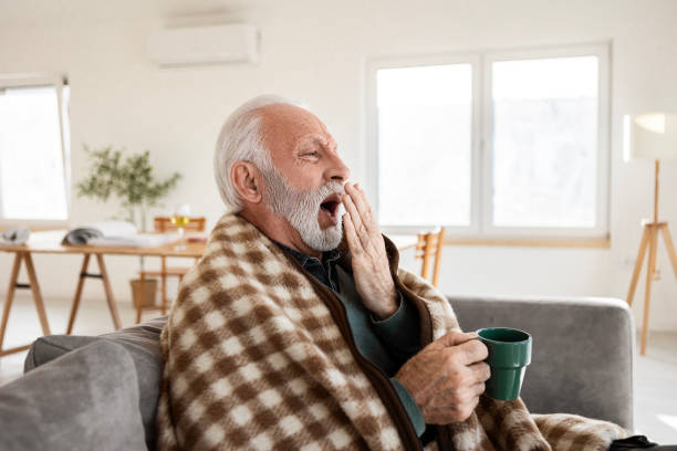 istock Elderly Man Wrapped in a Blanket with a Warm Drink Feeling Tired 2198393014