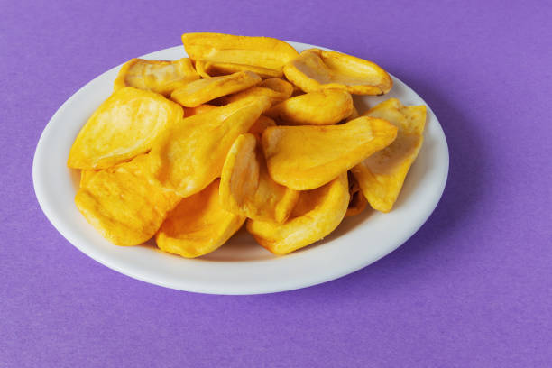 Keripik Sukun or Breadfruit Chips is a food made from breadfruit that is thinly sliced and fried until dry and crispy. Served on a white plate on a purple background