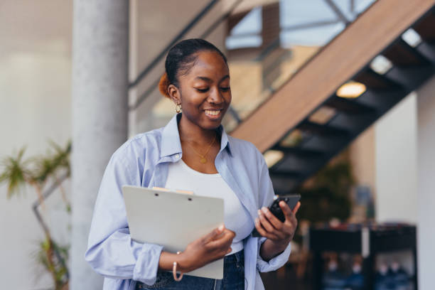 istock Young manager smiling and using smartphone and holding clipboard in modern office 2198394948