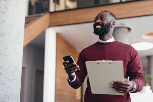 istock Smiling manager walking in office holding clipboard and smartphone 2198394996