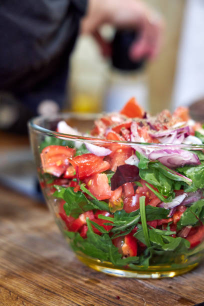 A woman stirring vegetable salad in a glass bowl, side view