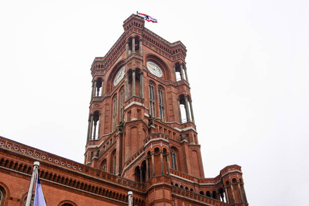 Berlin red town hall with Berlin flag flying in the cloudy sky. Detailed view of Rotes Rathaus clock tower, iconic landmark featuring ornate brickwork representing the city history. Copy space ayuntamiento rojo de berlín con la bandera de berlín ondeando en el cielo nublado. vista detallada de la torre del reloj rotes rathaus, un monumento emblemático con ladrillos ornamentados que representan la historia de la ciudad. espacio de copia