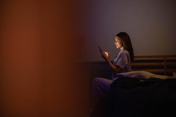 Woman Sitting in Bed at Night Using a Smartphone Under Dim Lighting