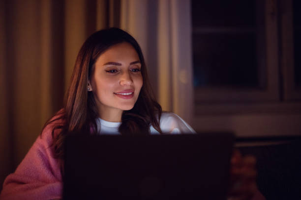 istock Smiling Woman Using Laptop Indoors During Evening Time at Home 2198405250