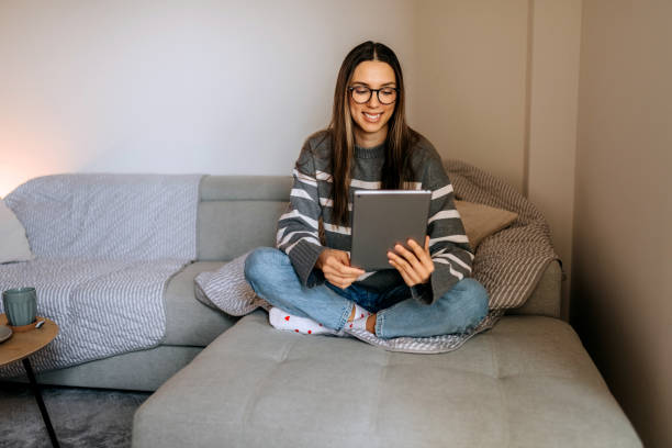 istock Young casually clothed woman using digital tablet while relaxing on a sofa at home 2198412840