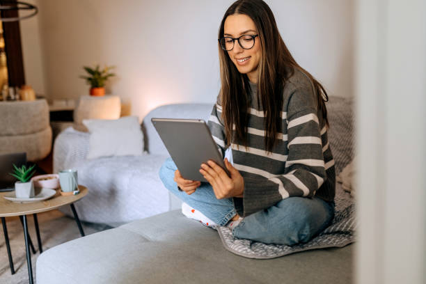 istock Young casually clothed woman using digital tablet while relaxing on a sofa at home 2198412846