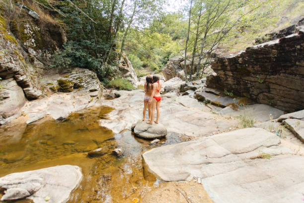 Two individuals explore a scenic, rocky creek surrounded by serene greenery, reflecting their enthusiasm for outdoor adventure and appreciation of nature. The setting radiates peace and natural vitality.