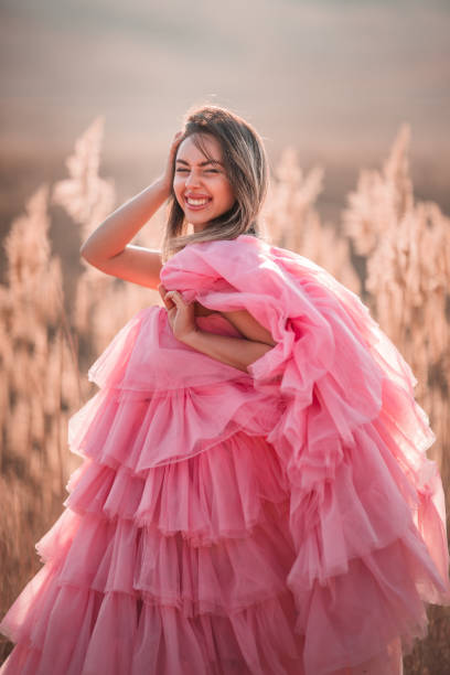 A woman stands in the winter fields wearing a pink fluffy dress.