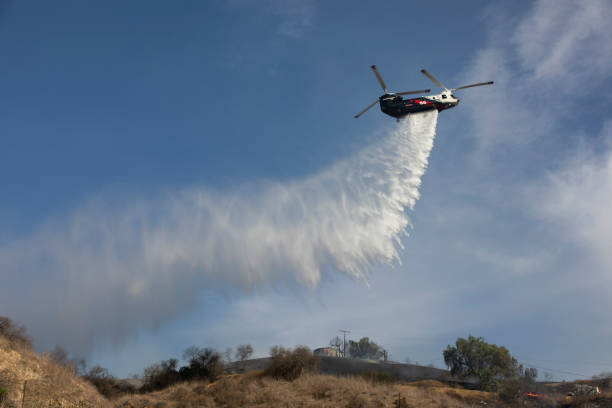 An aerial firefighting operation in action, with a firefighting helicopter carrying water to combat a raging wildfire
