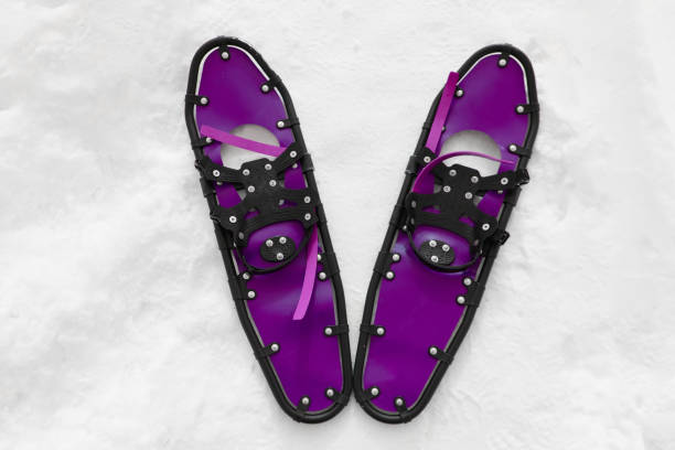 young sportsman walks in purple snowshoes and leggings on snow, close-up view of legs, winter hiking concept, active lifestyle