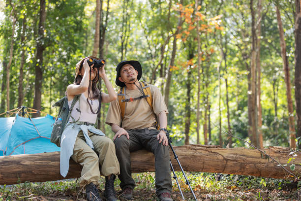 istock A couple of hikers sits on a fallen tree trunk in a dense forest, using binoculars for birdwatching. 2198443663
