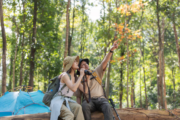 istock A couple of hikers sits on a fallen tree trunk in a dense forest, using binoculars for birdwatching. 2198443687