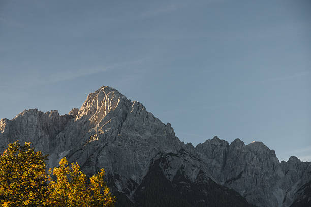 A striking view of the Dolomites bathed in the soft light of sunrise, highlighting the rugged peaks and serene atmosphere. Autumn leaves in the foreground add a touch of warmth and contrast to the dramatic rocky landscape. Perfect for showcasing the natural beauty of northern Italy.