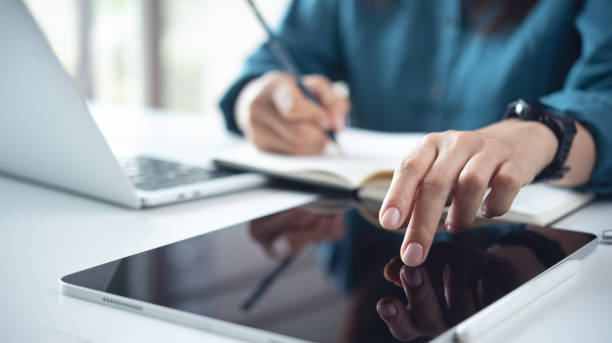 istock Woman using laptop computer searching ideas and making a note on notebook. Business woman working on laptop and planning, writing on notepad. Student studying online class, e-learning 2198453454