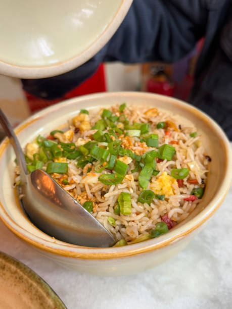 Stock photo of a tempting plate of egg fried rice with mixed vegetables, perfectly paired with crispy chicken strips glazed in a sweet and sour sauce. Bright peppers add crunch and color, enhancing this classic Chinese stir-fry dish
