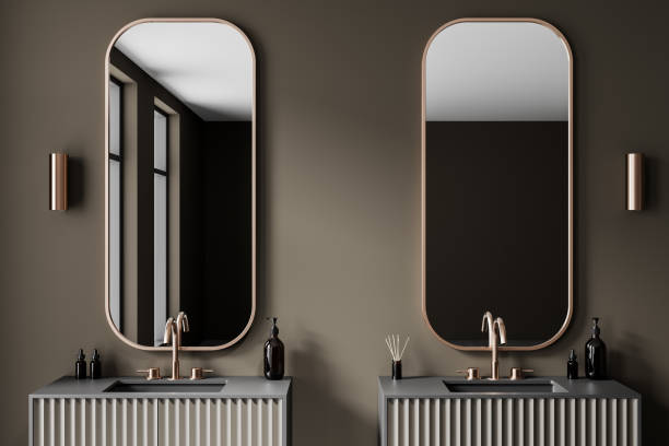 Modern bathroom with round mirrors and white sinks on wooden vanity against blue tiled wall. 3D Rendering