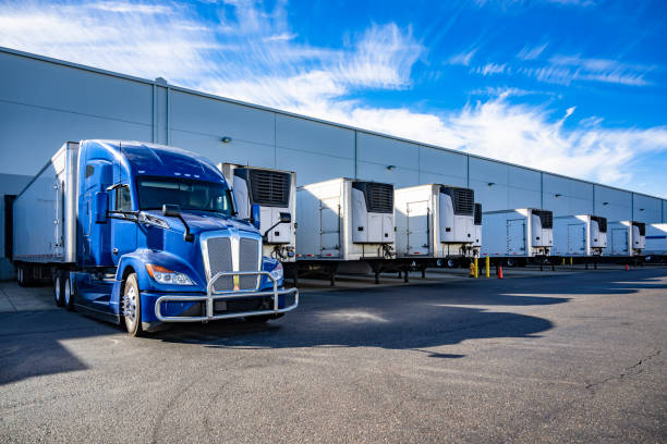 Big rig blue semi truck with refrigerator semi trailer standing in row with another semi trailers in warehouse dock gates loading cargo for the next freight stock photo